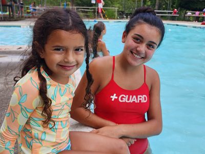 Image of a smiling lifeguard posing for a picture with a happy child at Coppermine Pool. Instructor leading a group swim lesson at the Coppermine 4 Seasons indoor pool, helping kids build confidence in the water.